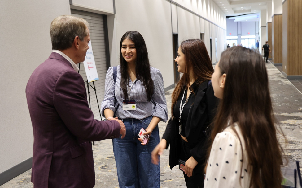 Gov. Pillen greets three female students participating in the Governor’s Youth Summit, shaking the hand of the student on the left.