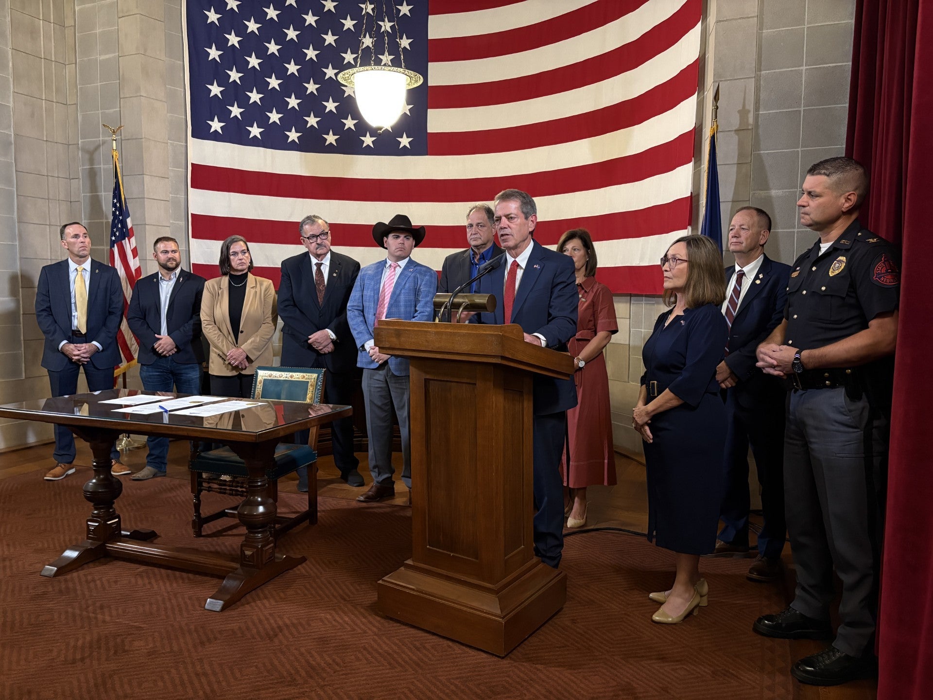 Gov. Jim Pillen addresses an audience while surrounded by his wife Suzanne Pillen, State Senators, and Agricultural Community members.