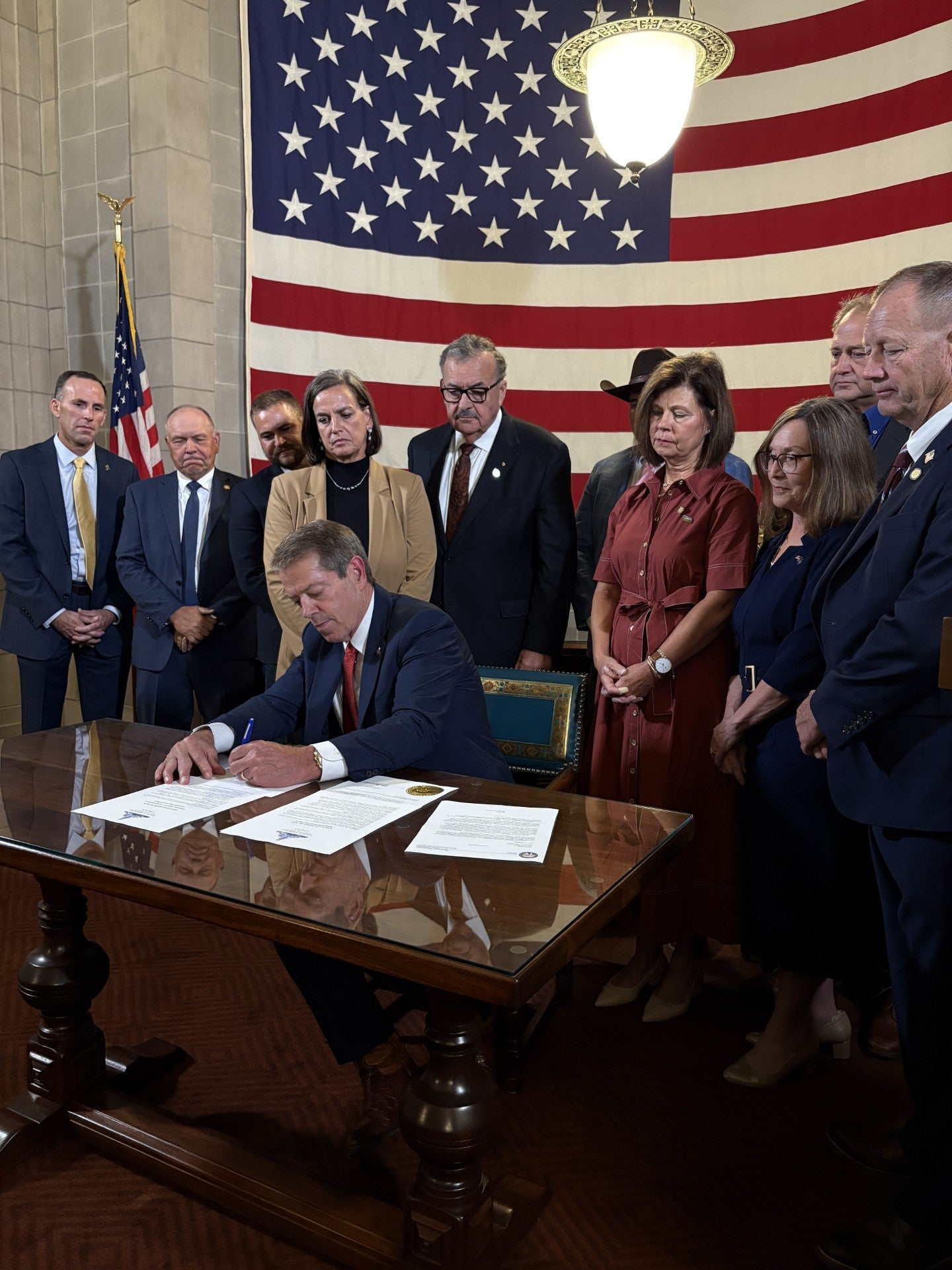 Gov. Jim Pillen signs Executive Order 26-21 while surrounded by his wife Suzanne Pillen, State Senators, and Agricultural Community members.