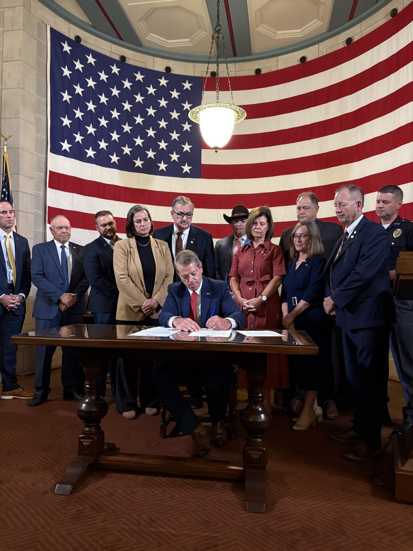Gov. Jim Pillen signs Executive Order 26-20 while surrounded by his wife Suzanne Pillen, State Senators, and Agricultural Community members.