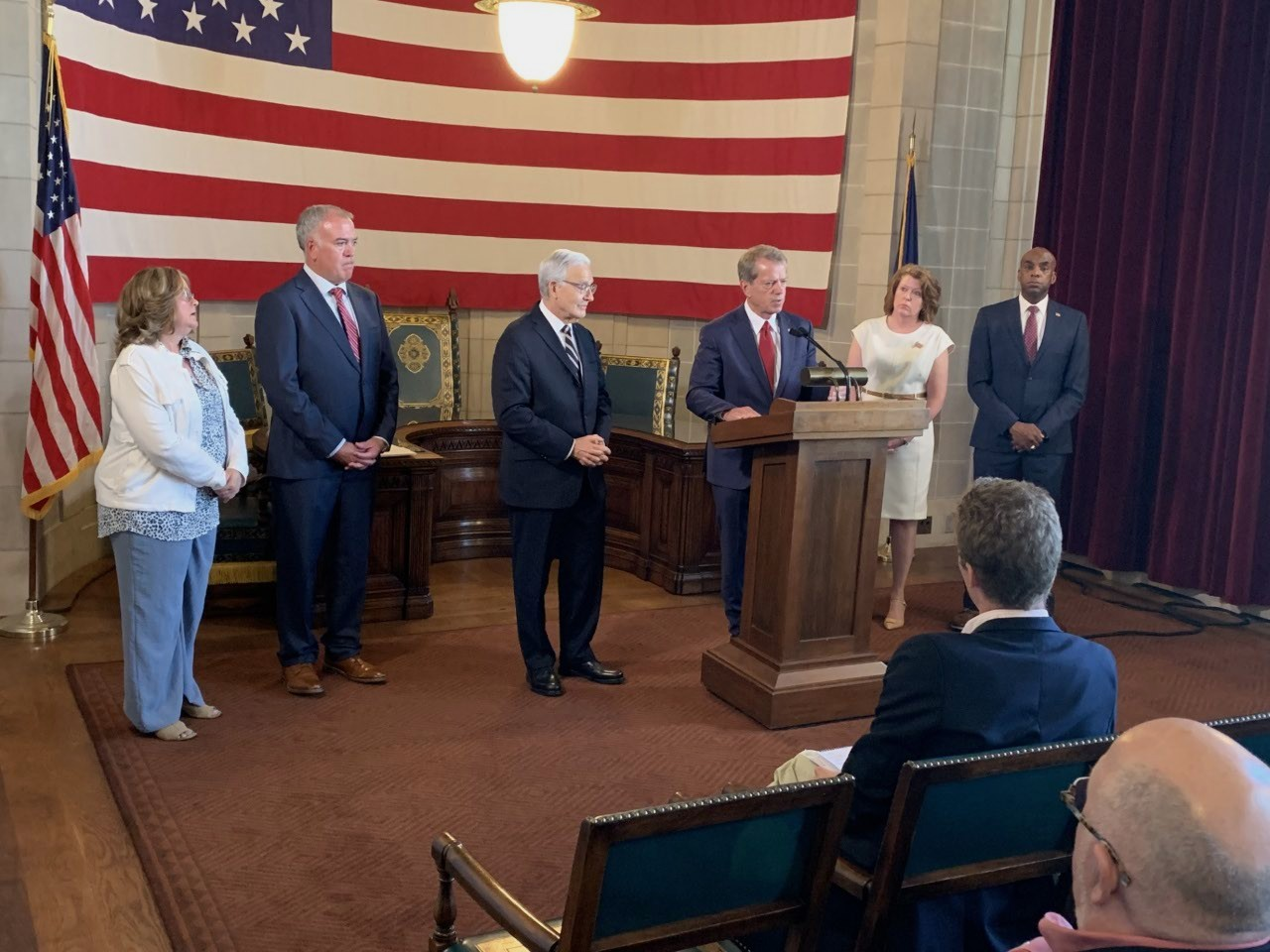 Governor Jim Pillen speaks on integrity in the ballot petition process. He is joined by Secretary of State Bob Evnen, and county election officials. In the background is a a large American flag.