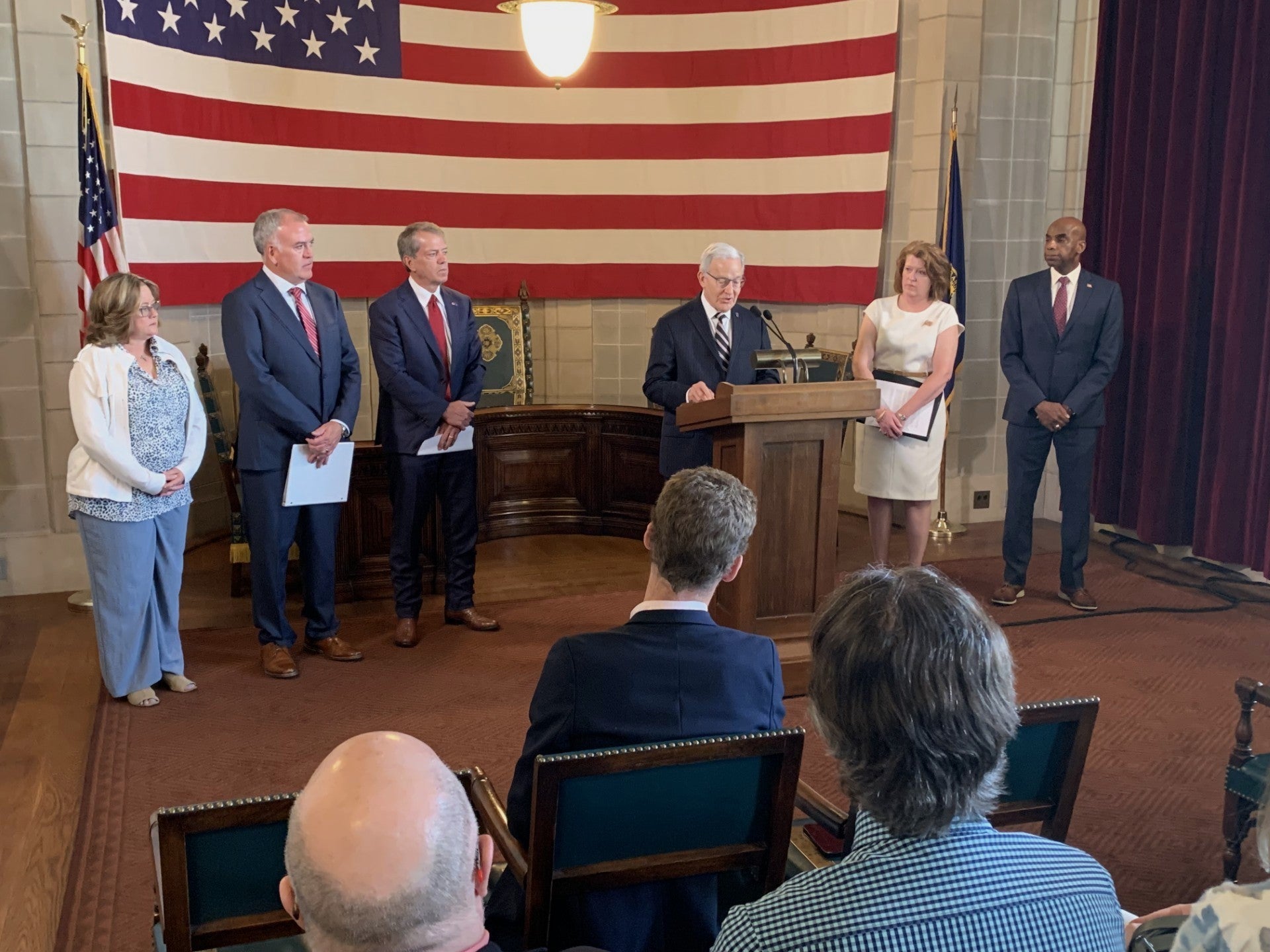 Secretary of State Bob Evnen recognizes county election workers. He is joined by Governor Jim Pillen and county election officials. In the background is a a large American flag.