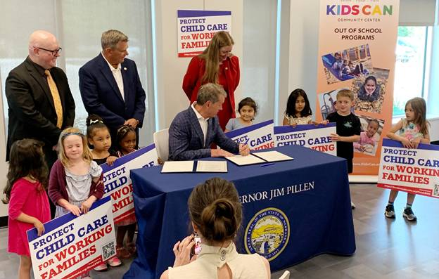 Governor Jim Pillen signs LB 304 surrounded by children and State representatives at the Kids Can Community Center in Omaha.