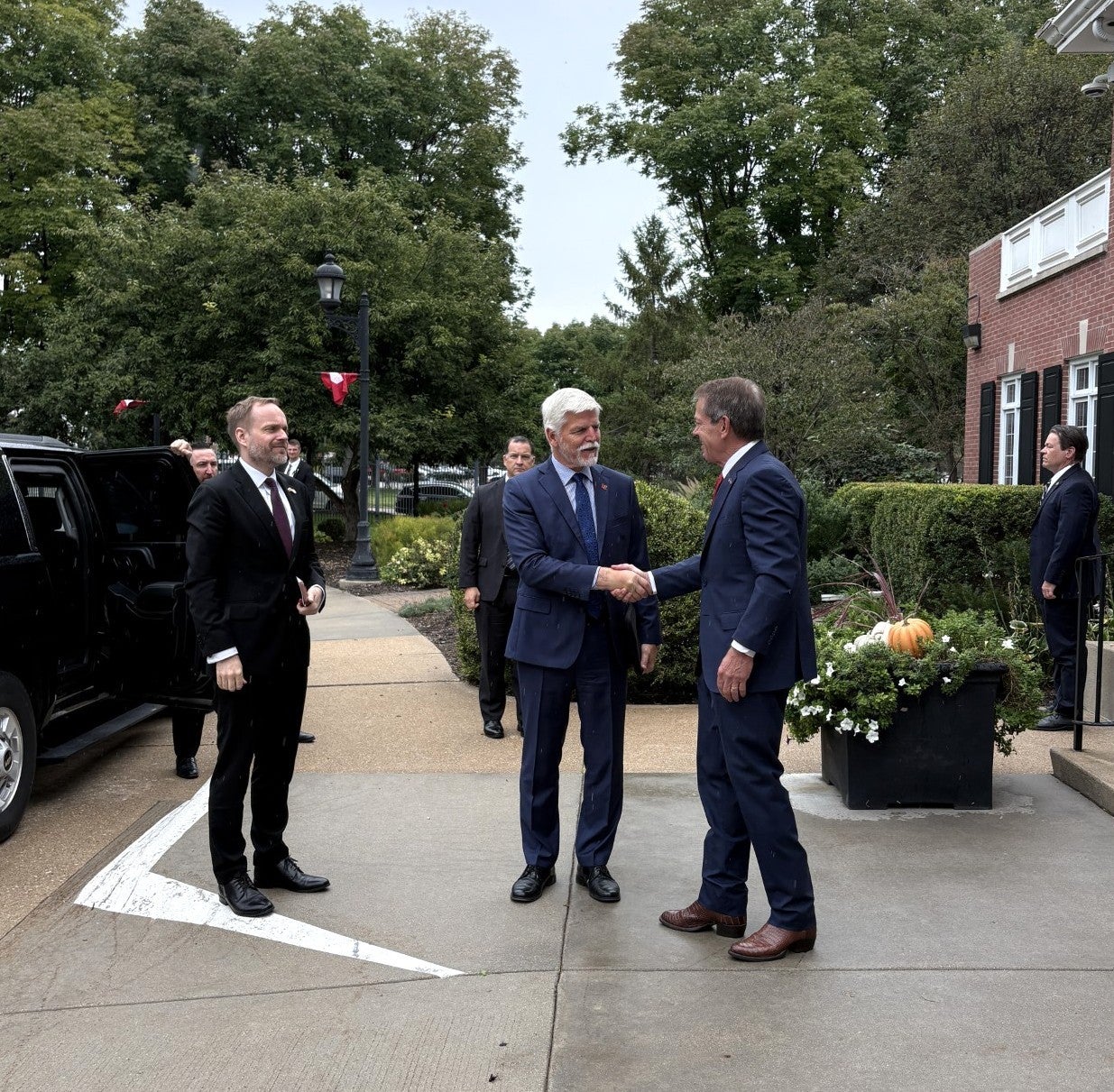 Gov. Jim Pillen shakes hands with Petr Pavel, President of the Czech Republic outside the Governor's Mansion. Jakub Kulhánek, Ambassador of the Czech Republic and other members of the detail stand beside a limousine as they look on.