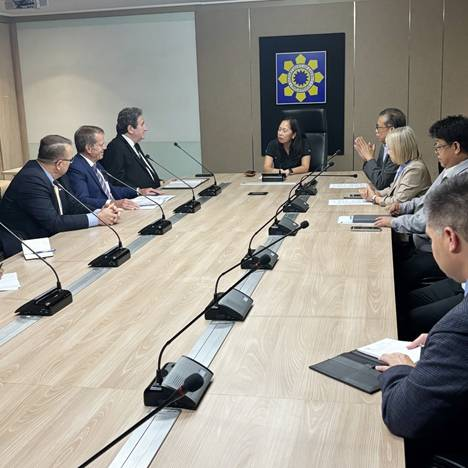 Gov. Pillen and other unnamed delegation members sitting at a table with microphones meet with Sharon Garin, Secretary of the Philippines Department of Energy.