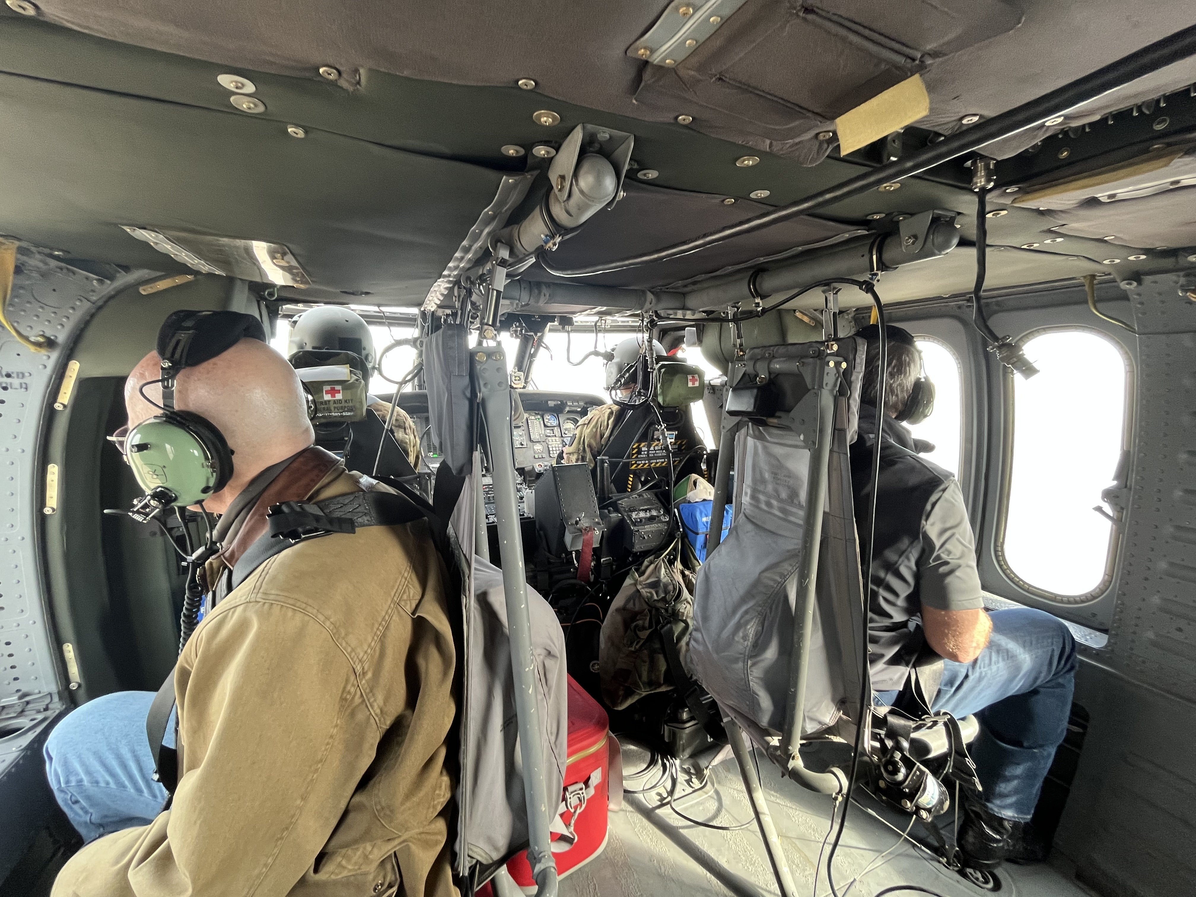 US Senator Ricketts, left, and Governor Pillen, right, and National Guard airmen, front, survey the land from a National Guard helicopter.