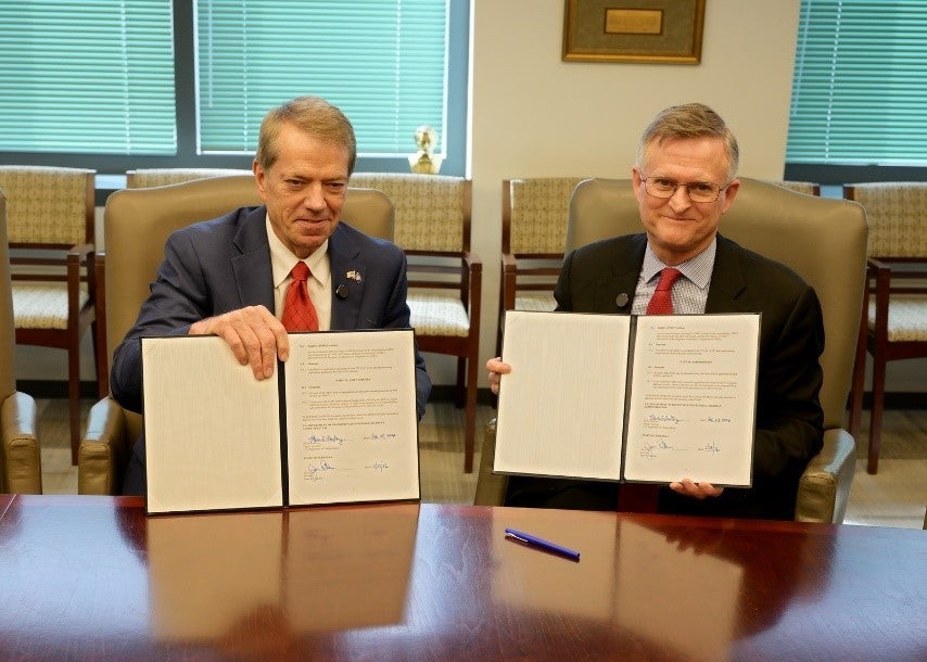 Governor Jim Pillen and U.S. Transportation Secretary Sean P. Duffy, sitting behind a desk, display sign copies of a new agreement with Nebraska through the Federal Highway Administration (FHWA).