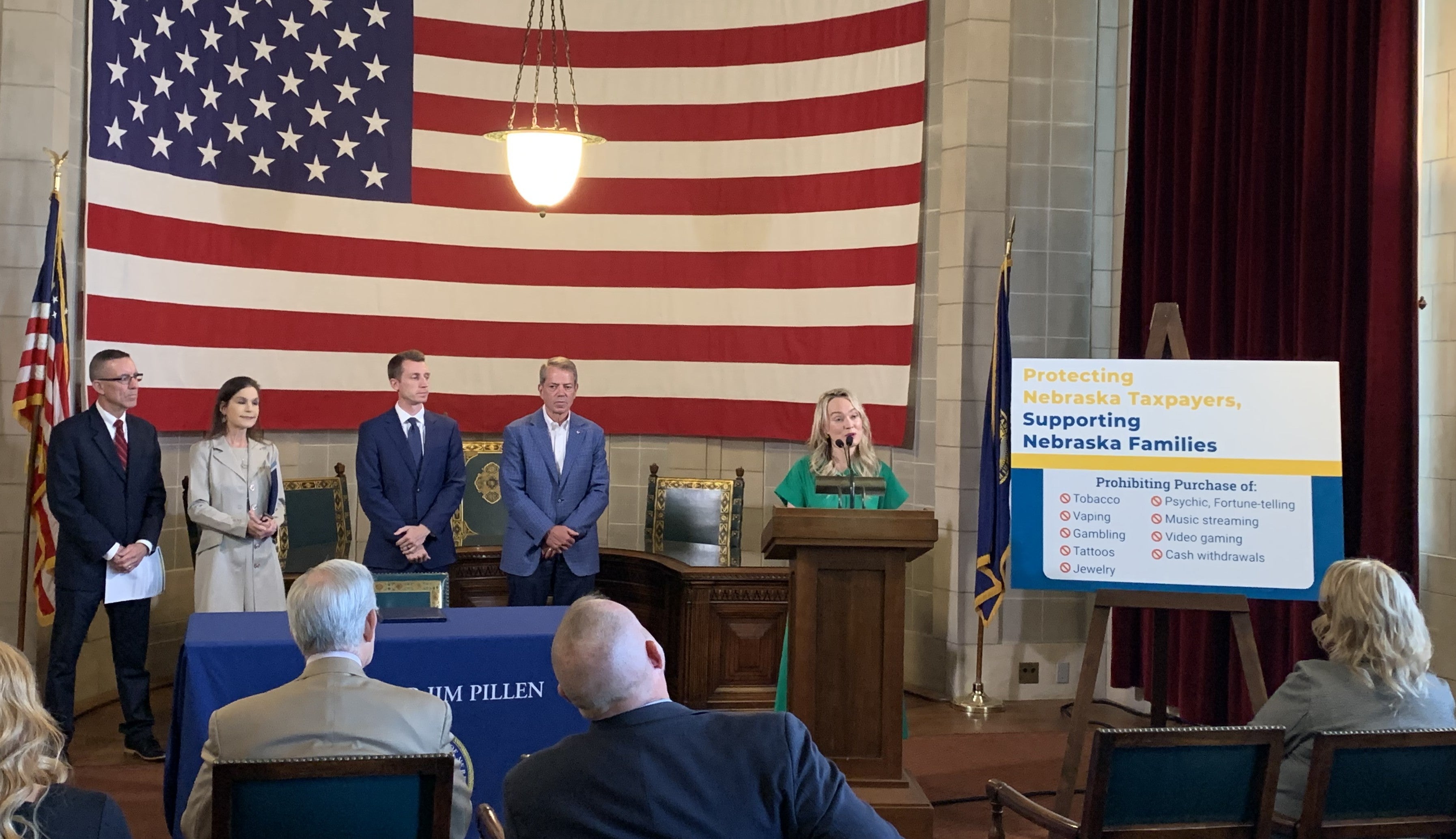 MiMi Greene state government affairs director for the Foundation for Government Accountability addresses the audience. Others flanking her at the podium are DHHS CEO Dr. Steve Corsi, Governor Pillen, and Barbara Lacina.